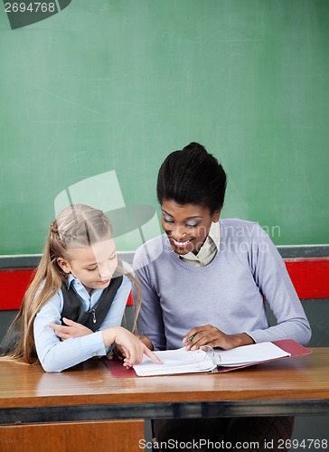 Image of Schoolgirl Pointing In Binder With Teacher At Desk