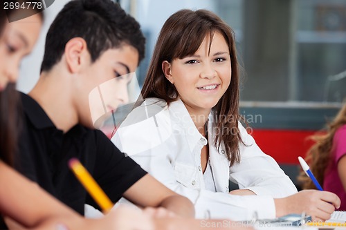 Image of Teenage Schoolgirl Smiling With Friends In Classroom