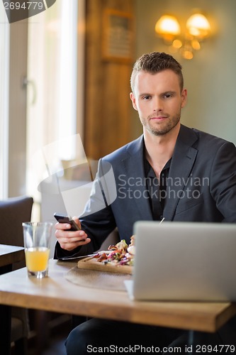 Image of Businessman With Mobilephone And Laptop Having Food