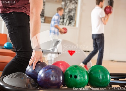 Image of Man Picking Bowling Ball With Friends in Background