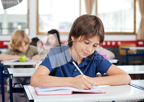 Image of Schoolboy Writing In Book At Desk