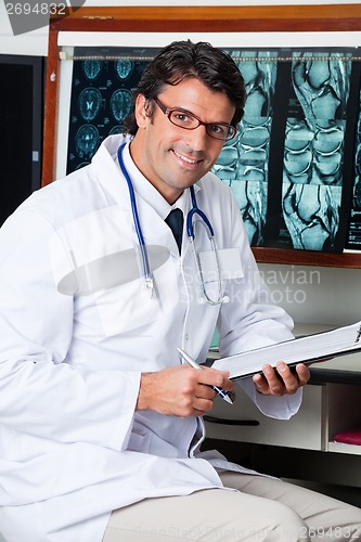 Image of Doctor Sitting At Desk With Clipboard