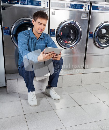 Image of Man Using Digital Tablet While Sitting Against Washing Machines