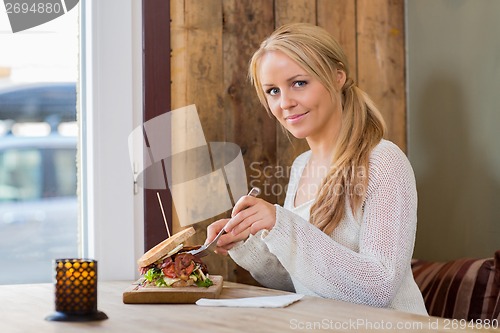 Image of Young Woman Eating Sandwich At Cafe