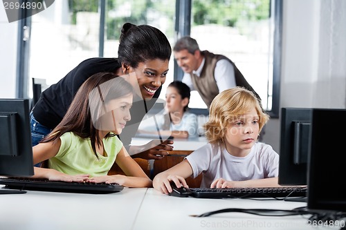 Image of Female Teacher Assisting Schoolchildren In Using Computer