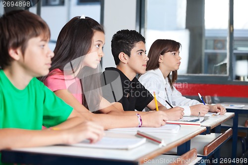 Image of Teenage Students Looking Away While Studying At Desk