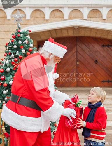 Image of Boy Looking At Santa Claus While Taking Gift From Him