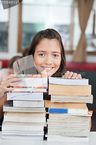 Image of Schoolgirl Leaning On Stack Of Books In Classroom