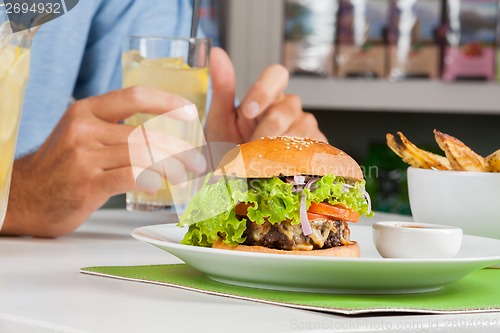 Image of Burger With Man's Hand Holding Drink At Table