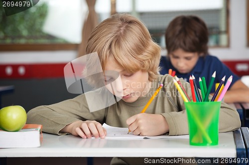 Image of Schoolboy Writing In Book At Desk