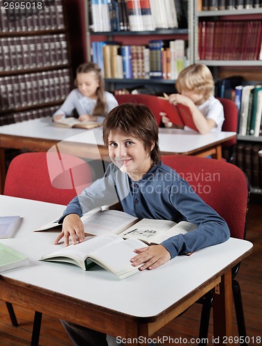 Image of Boy Sitting At Table With Books With Classmates In Background