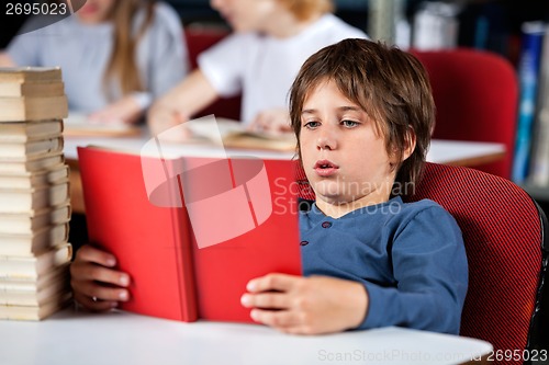 Image of Relaxed Boy Reading Book At Table In Library