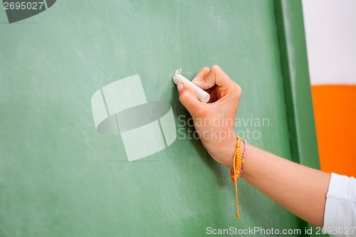 Image of Girl's Hand Writing On Green Chalkboard In Kindergarten