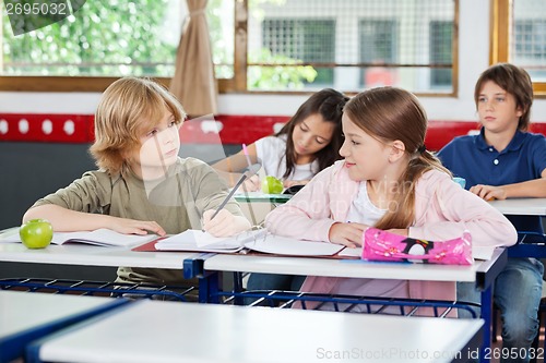 Image of Schoolboy Looking At Girl While Writing At Desk