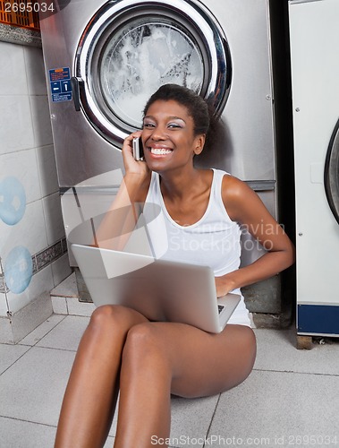 Image of Woman Using Laptop And Mobilephone In Laundromat