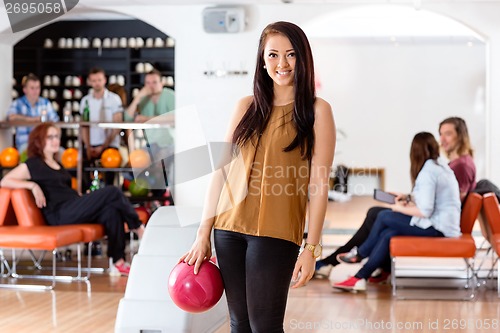 Image of Happy Young Woman Holding Bowling Ball in Club