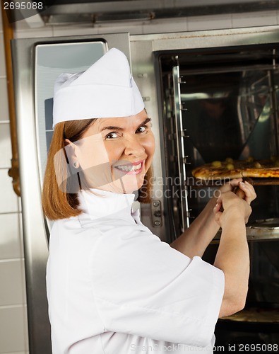 Image of Mature Female Chef Placing Pizza In Oven