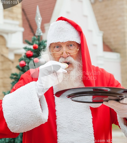 Image of Santa Claus Eating Cookie Against House