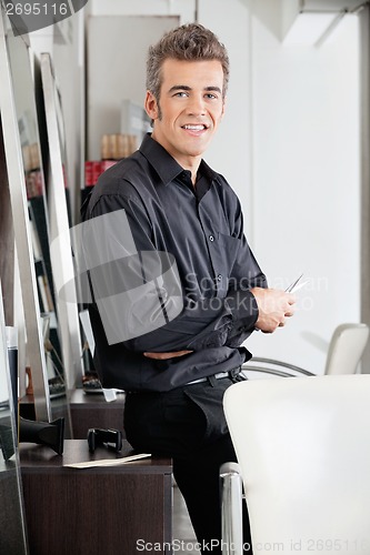 Image of Male Hairstylist With Scissors Leaning On Cabinet