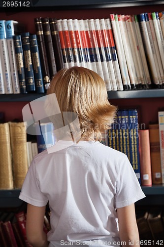 Image of Schoolboy Standing Against Bookshelf In Library