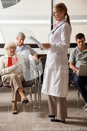 Image of Doctor Reading File With People In Lobby