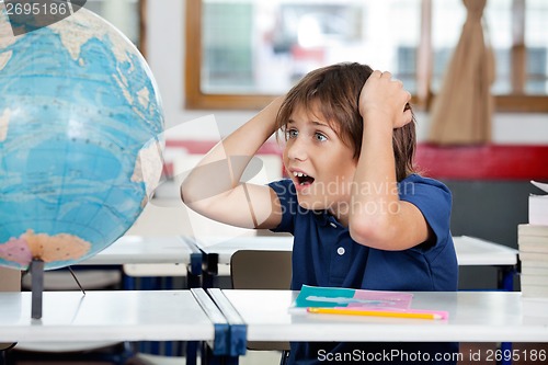 Image of Shocked Schoolboy Looking At Globe In Classroom