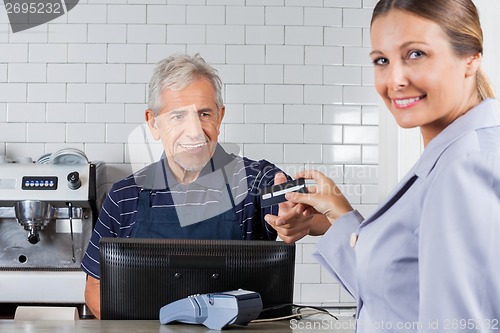 Image of Female Customer Giving Credit Card To Senior Cashier