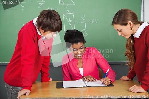 Image of Teacher Writing In Binder While Students Standing At Desk