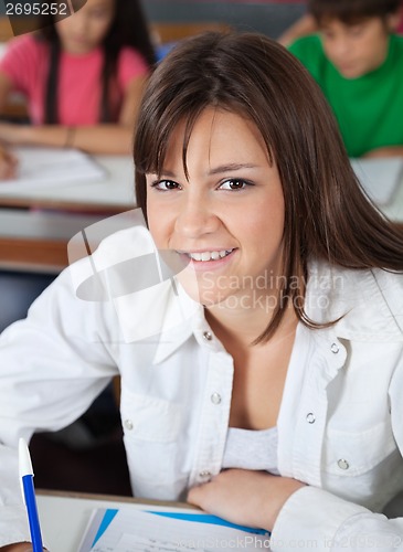 Image of Schoolgirl Sitting At Desk With Classmates In Background