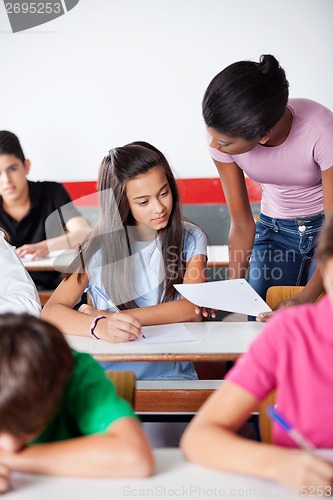 Image of Female Teacher Showing Paper To Female Student At Desk