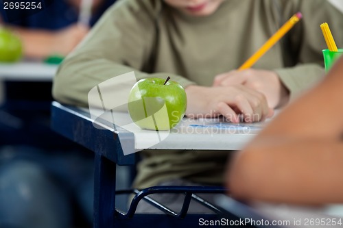 Image of Schoolboy Writing In Book With Apple At Desk