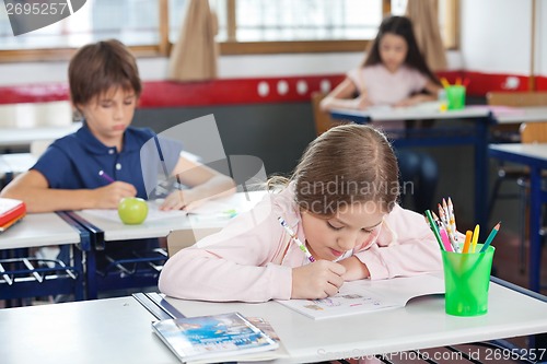 Image of Schoolgirl Drawing While Leaning On Desk In Classroom