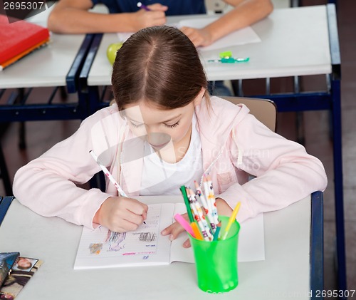 Image of Schoolgirl Drawing At Desk In Classroom