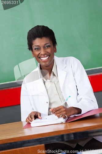 Image of Happy Teacher With Pen And Binder Sitting At Desk