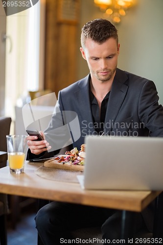 Image of Businessman With Cellphone And Laptop In Restaurant