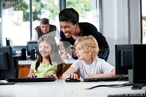 Image of Happy Teacher Assisting Schoolchildren In Using Computer