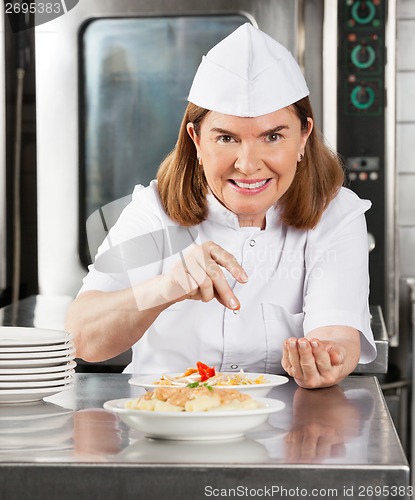 Image of Mature Female Chef Garnishing Dish