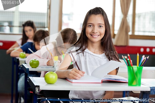 Image of Schoolgirl Writing In Book At Classroom