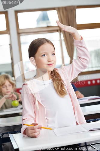 Image of Schoolgirl Looking Away While Raising Hand In Classroom