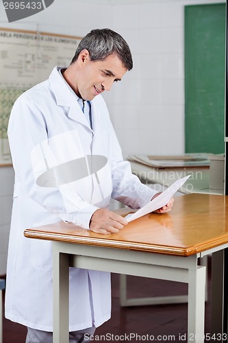 Image of Male Teacher Reading Paper At Desk