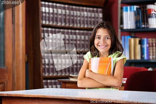 Image of Schoolgirl Holding Book While Sitting At Table In Library