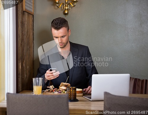 Image of Businessman Messaging On Mobilephone While Having Meal In Cafe