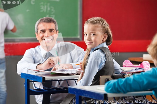 Image of Girl And Teacher Sitting At Desk In Classroom