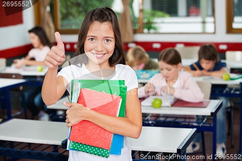 Image of Schoolgirl Gesturing Thumbs Up While Holding Books