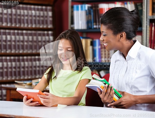 Image of Librarian And Schoolgirl Looking Together At Book In Library