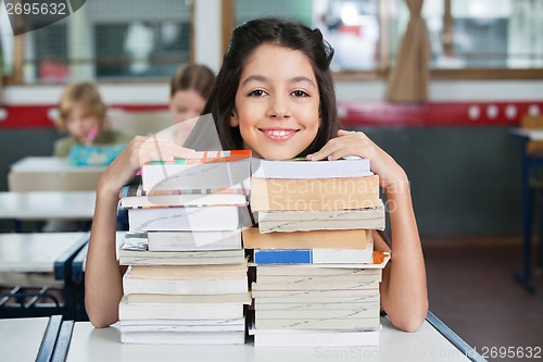 Image of Happy Schoolgirl Resting Chin On Stacked Books At Desk