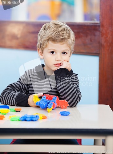 Image of Bored Boy Holding Blocks Sitting At Desk In Classroom