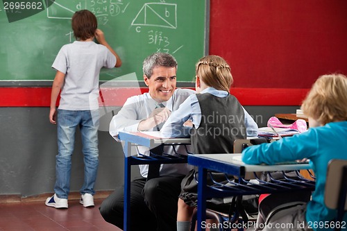 Image of Teacher Looking At Schoolgirl While Crouching At Desk