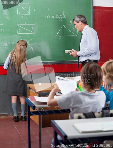 Image of Rear View Of Little Schoolgirl Writing On Board