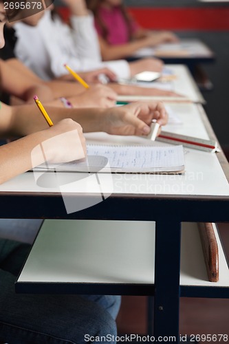 Image of Schoolchildren Writing In A Row At Desk In Classroom